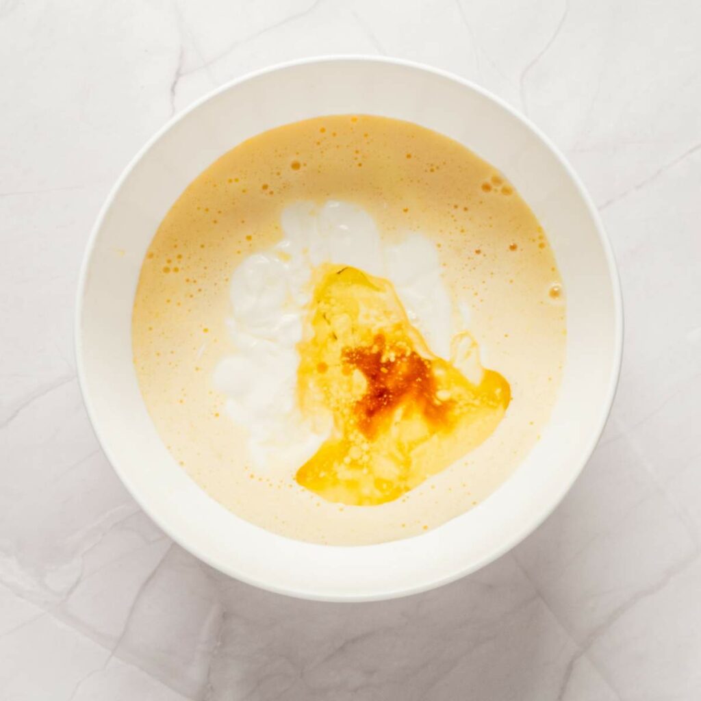 A white bowl containing a creamy orange mixture with white yogurt and a splash of oil or sauce on top.