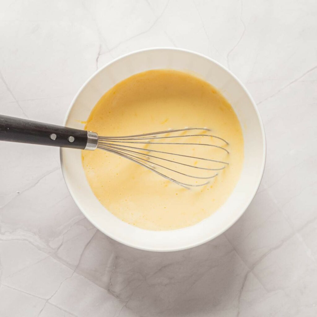 A white bowl filled with a creamy yellow mixture is on a light marble surface.