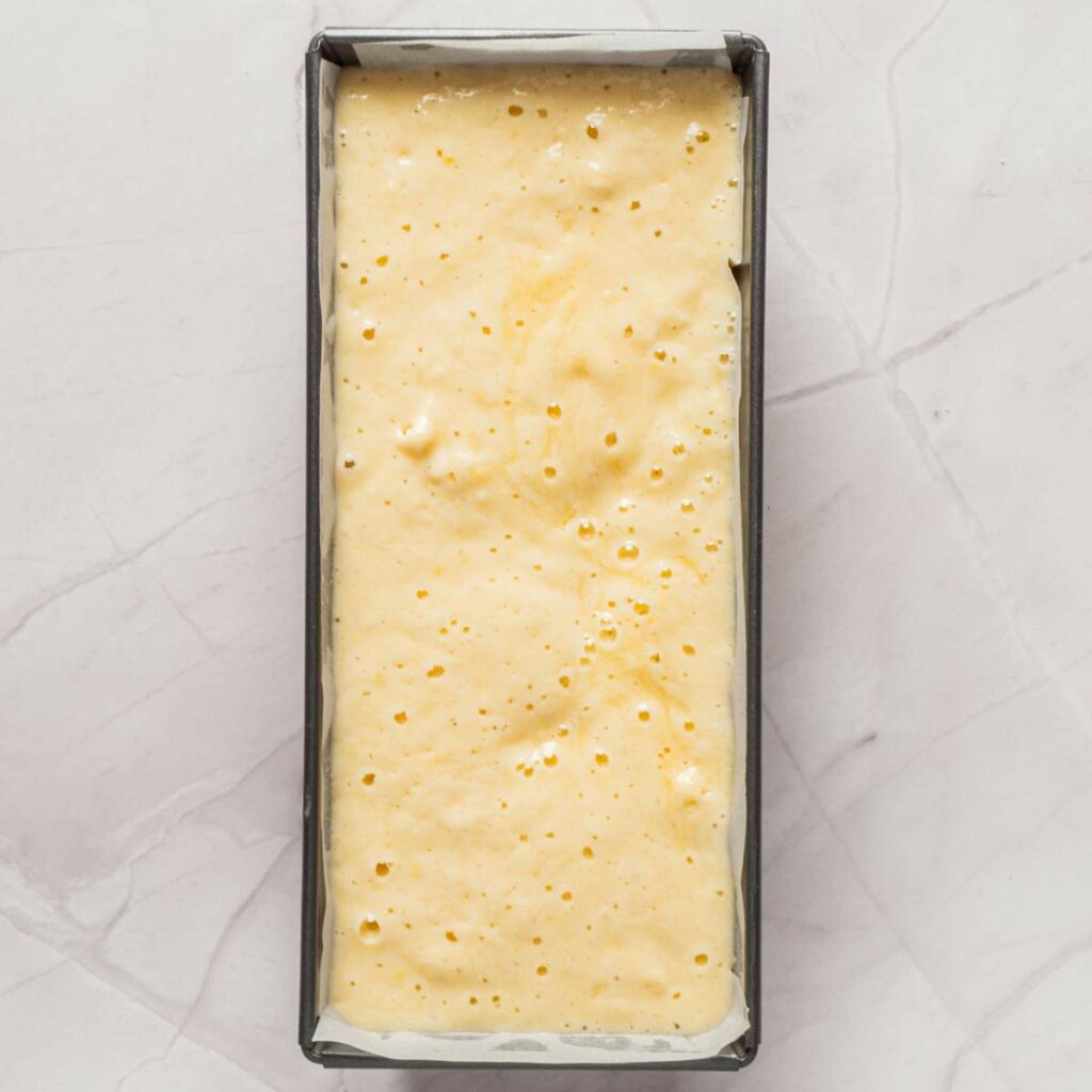 Loaf pan filled with unbaked yellow batter on a gray marble surface.