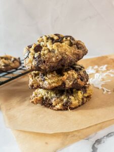 Three magic cookies stacked on a piece of parchment paper with another cookie on a cooling rack in the background.