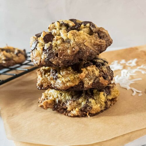 Three magic cookies stacked on a piece of parchment paper with another cookie on a cooling rack in the background.