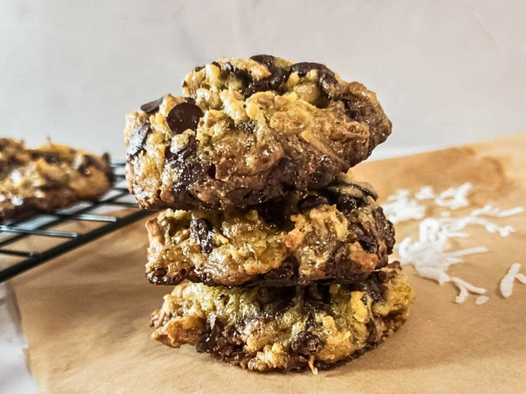 Magic cookies stacked on parchment paper, with a cooling rack and some shredded coconut in the background.
