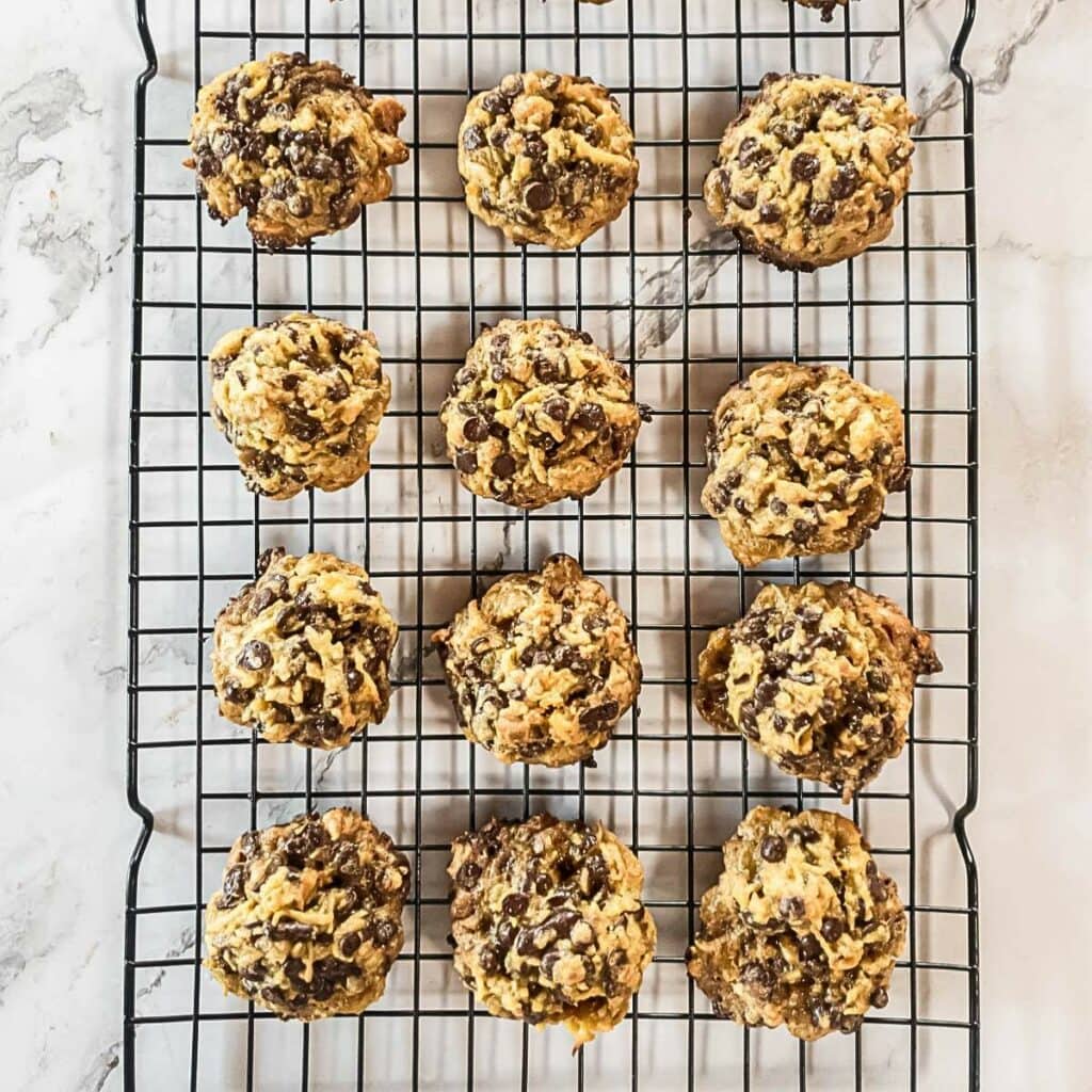 Chocolate chip cookies cooling on a wire rack, arranged in four rows, on a marble surface.