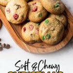 Wooden tray with soft, chewy cookies containing red and green M&Ms, placed on a white marble surface.