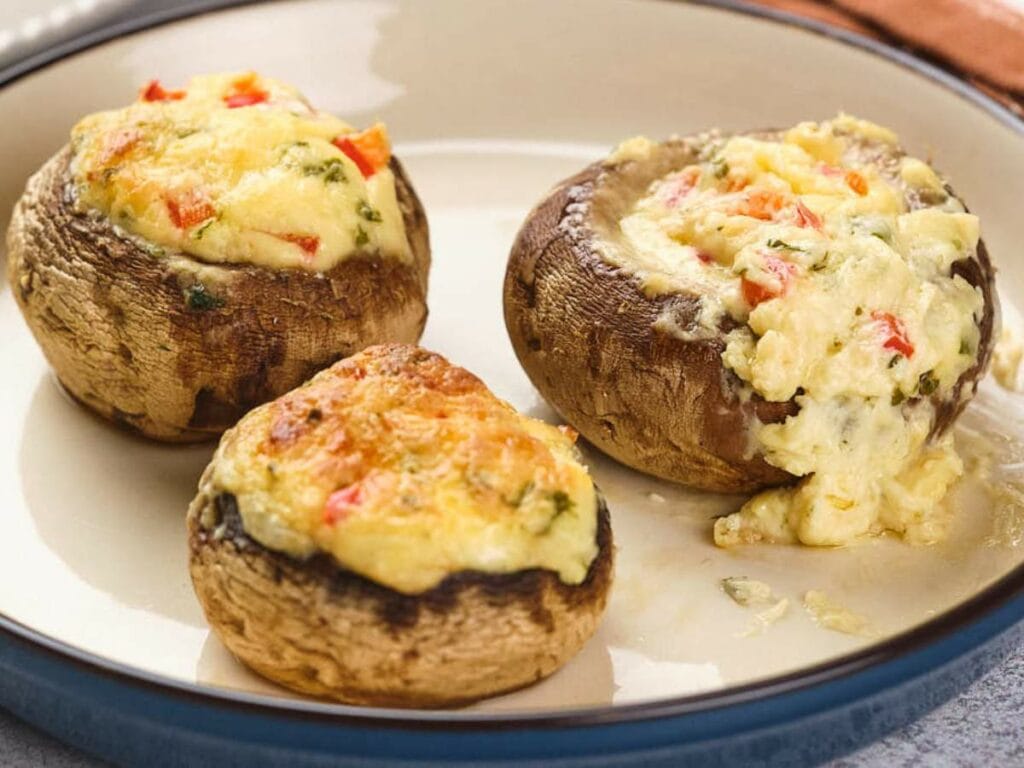 Three stuffed mushrooms filled with cheese and herbs on a beige plate.