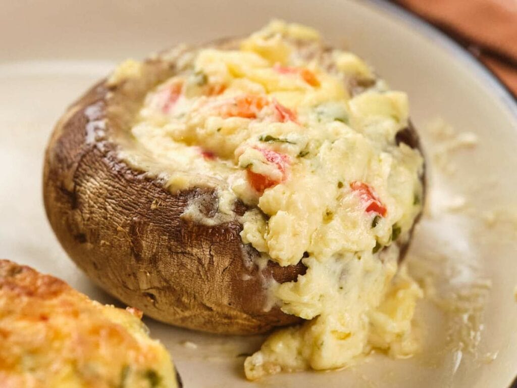Stuffed mushroom cap overflowing with a creamy mixture of cheese and chopped red and green vegetables on a plate.