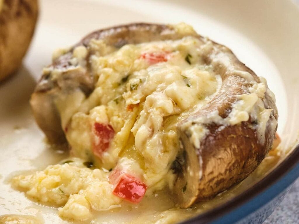 Close-up of a stuffed mushroom cap filled with melted cheese and chopped red pepper, served on a white plate.