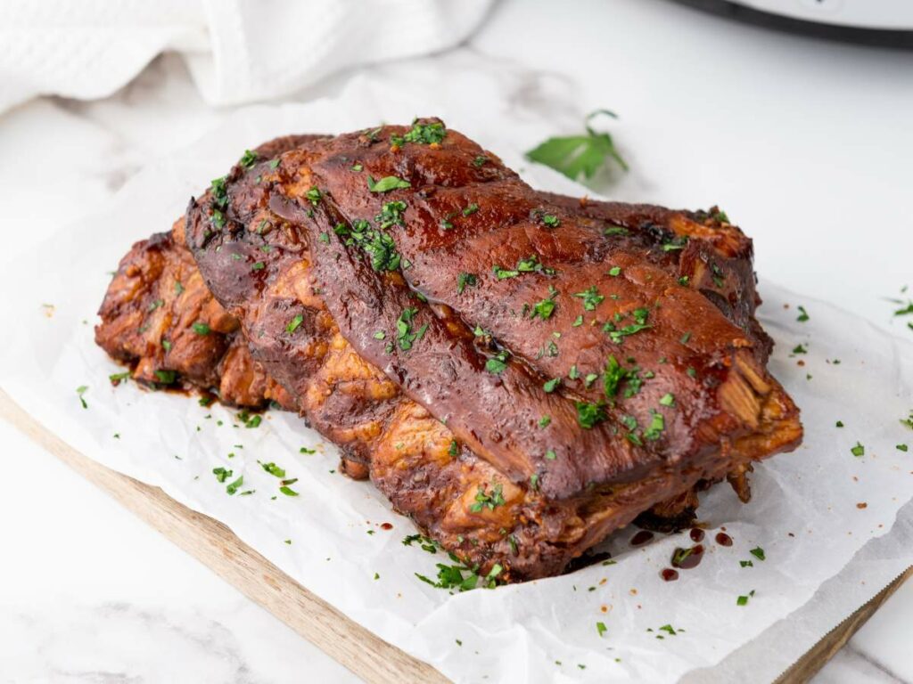 Cooked baby back ribs garnished with chopped herbs, placed on parchment paper on a wooden board.