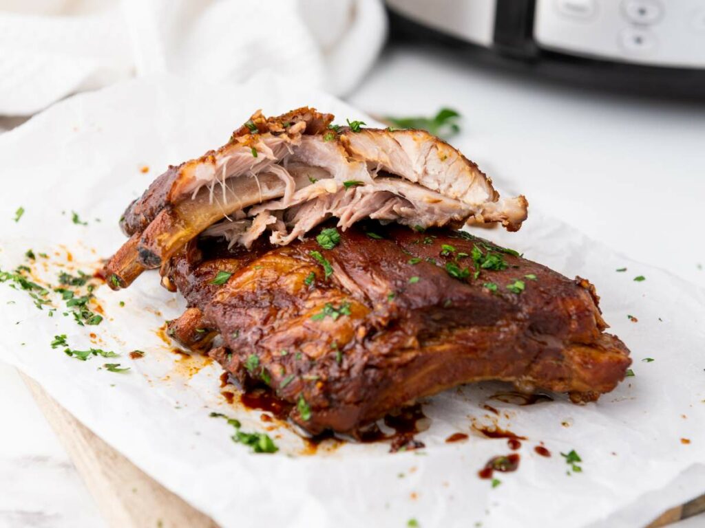 Baby back ribs with a caramelized glaze are garnished with chopped herbs.