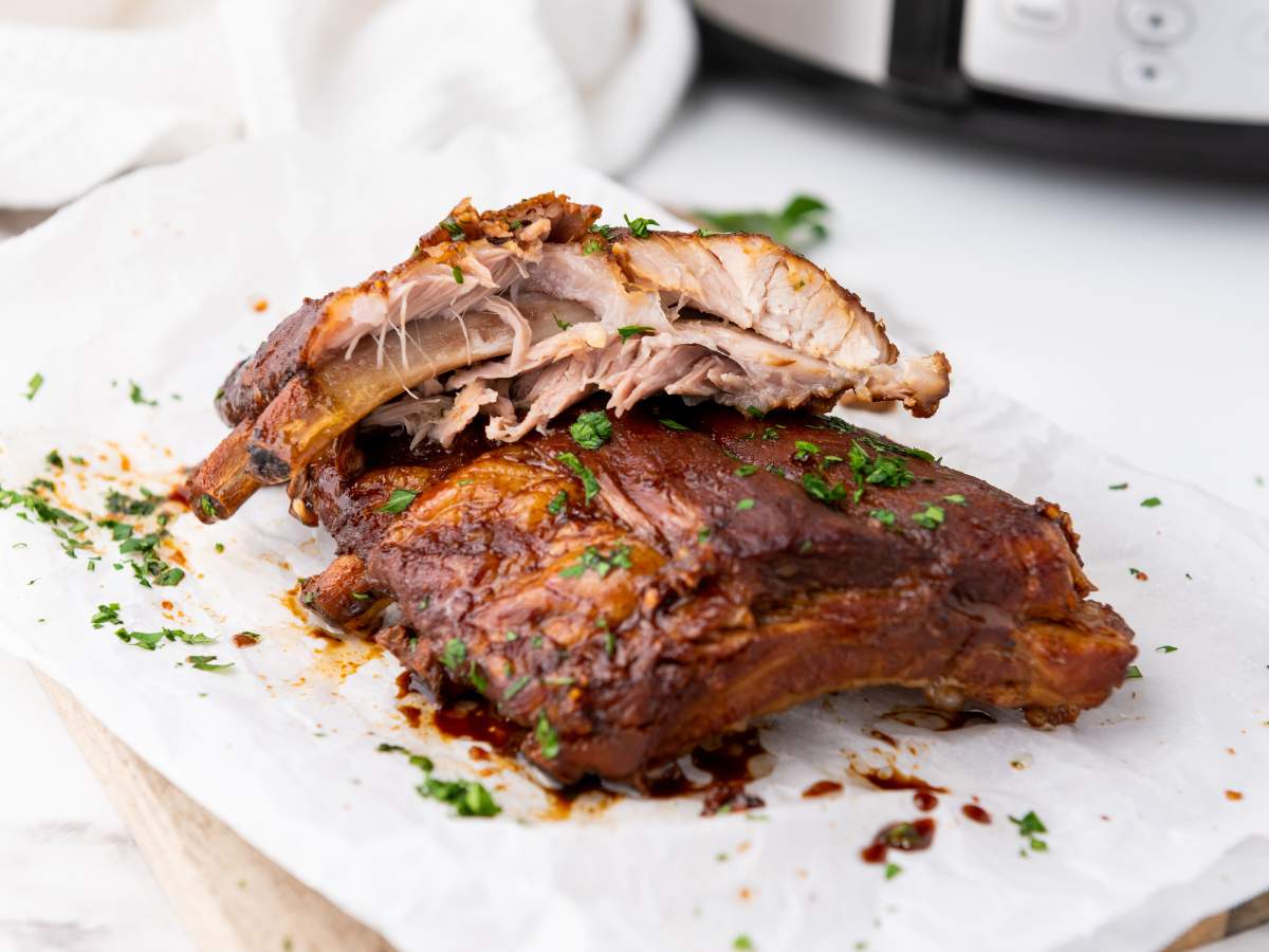 Baby back ribs with a caramelized glaze are garnished with chopped herbs.