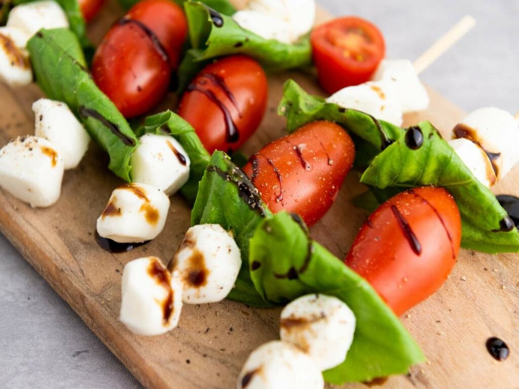 basil tomato mozzarella skewers drizzled with balsamic glaze on a wooden board.