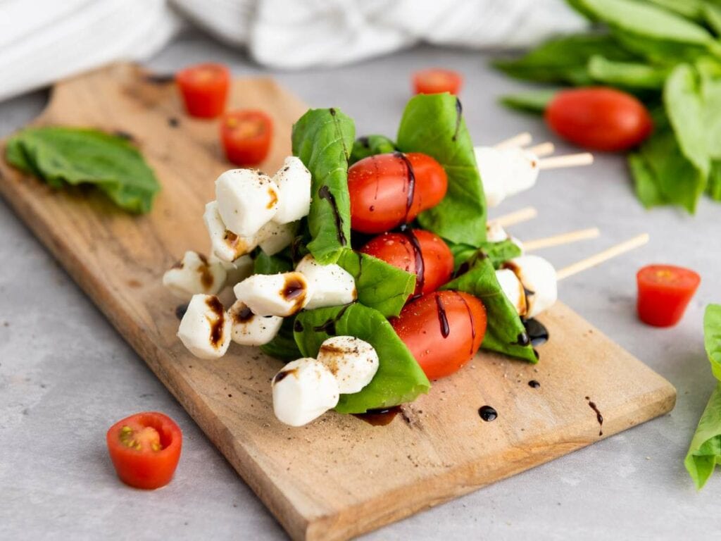 Basil tomato mozzarella skewers on a wooden board, drizzled with balsamic glaze.