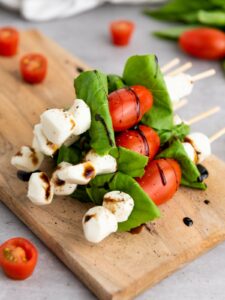 Skewers with cherry tomatoes, mozzarella balls, and basil leaves on a wooden board, drizzled with balsamic glaze.