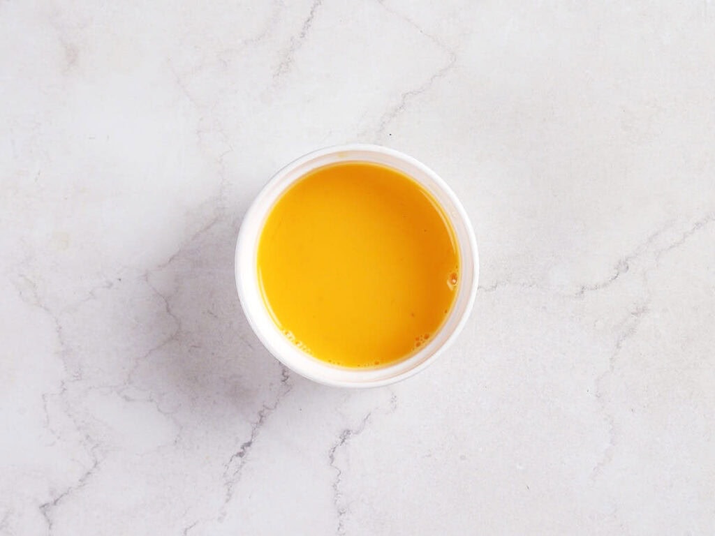A small white cup filled with bright orange-yellow liquid, placed on a light-colored marble surface.