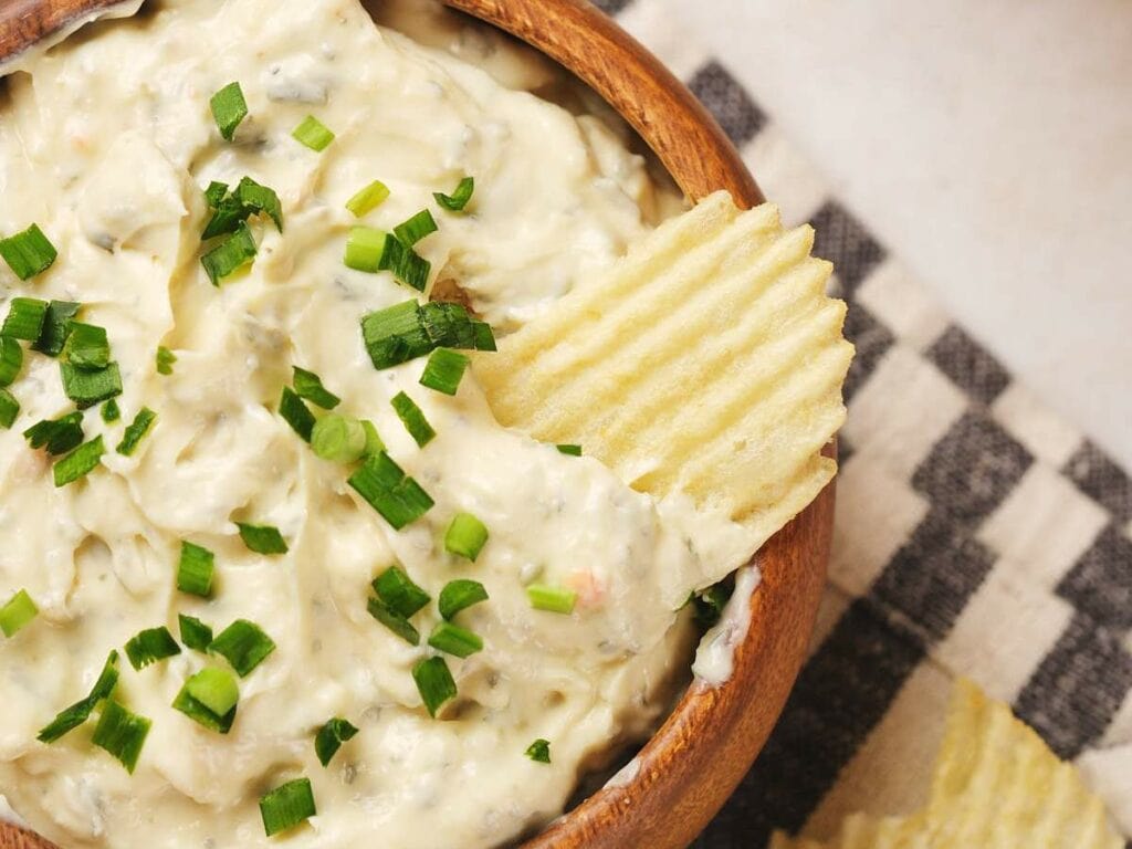 A wooden bowl filled with creamy chip dip topped with chopped green onions.