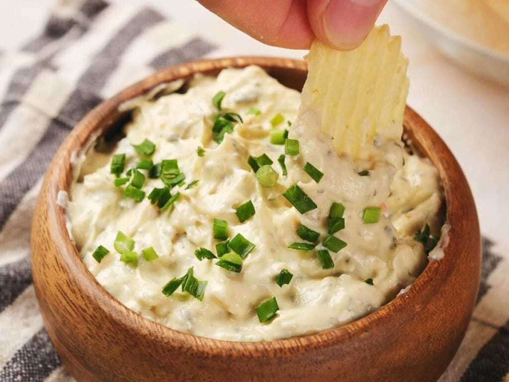 A ridged chip is being dipped into a bowl of creamy chip dip topped with chopped green onions.