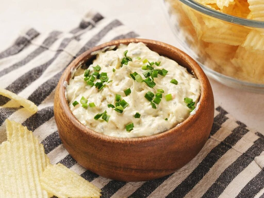 A wooden bowl filled with creamy chip dip topped with chopped chives.
