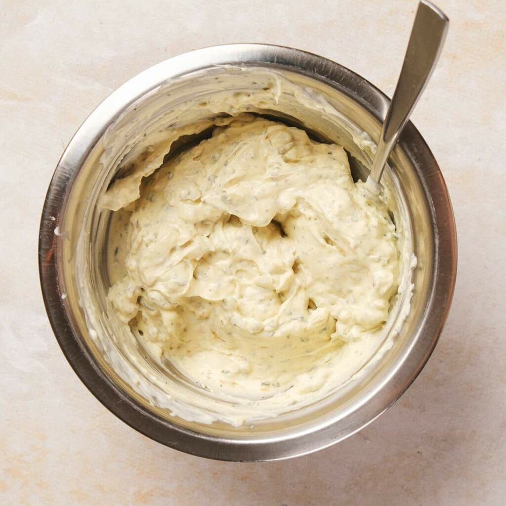 A stainless steel bowl filled with a creamy mixture and a spoon rests on a light marble surface.