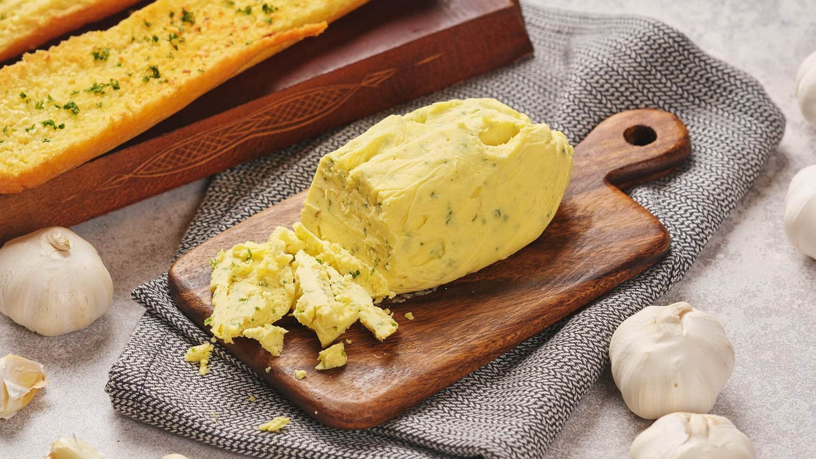 A block of garlic herb butter partially sliced on a wooden board.