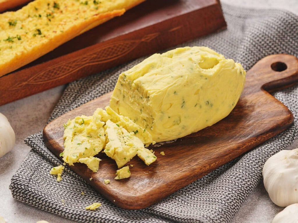 A block of garlic butter with pieces broken off sits on a wooden board.