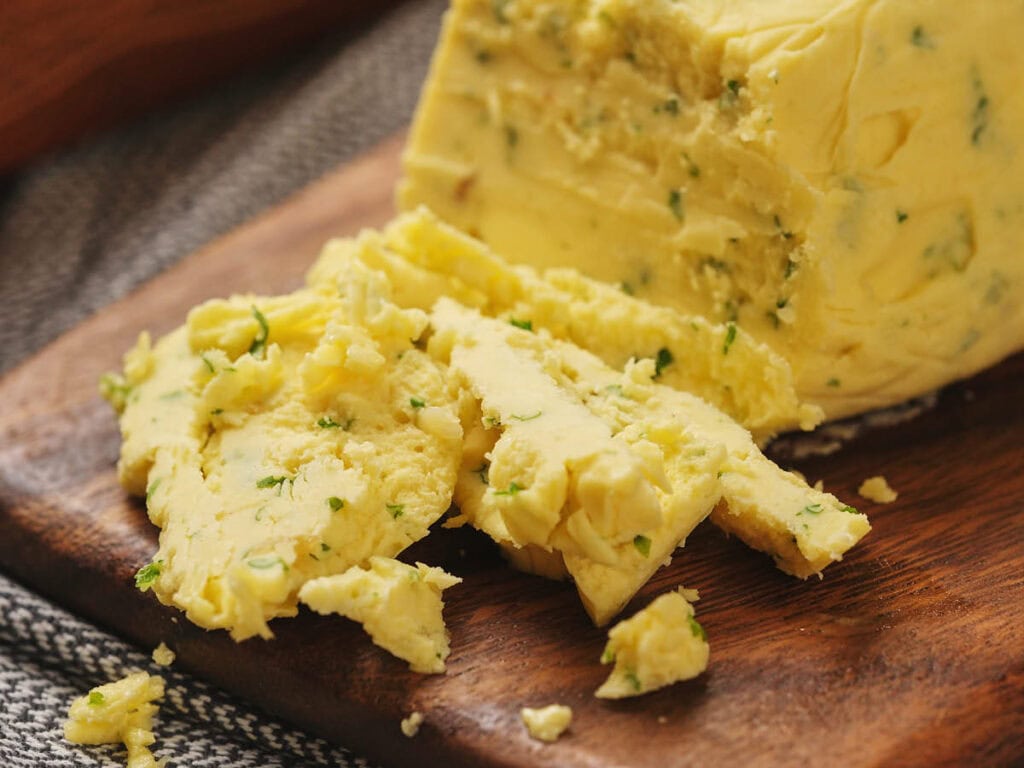 A block of garlic butter partially sliced on a wooden cutting board.