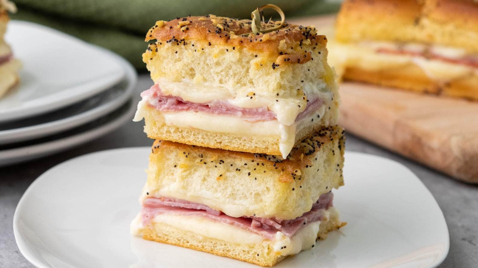 Two stacked slices of ham and cheese sliders placed on a white plate.