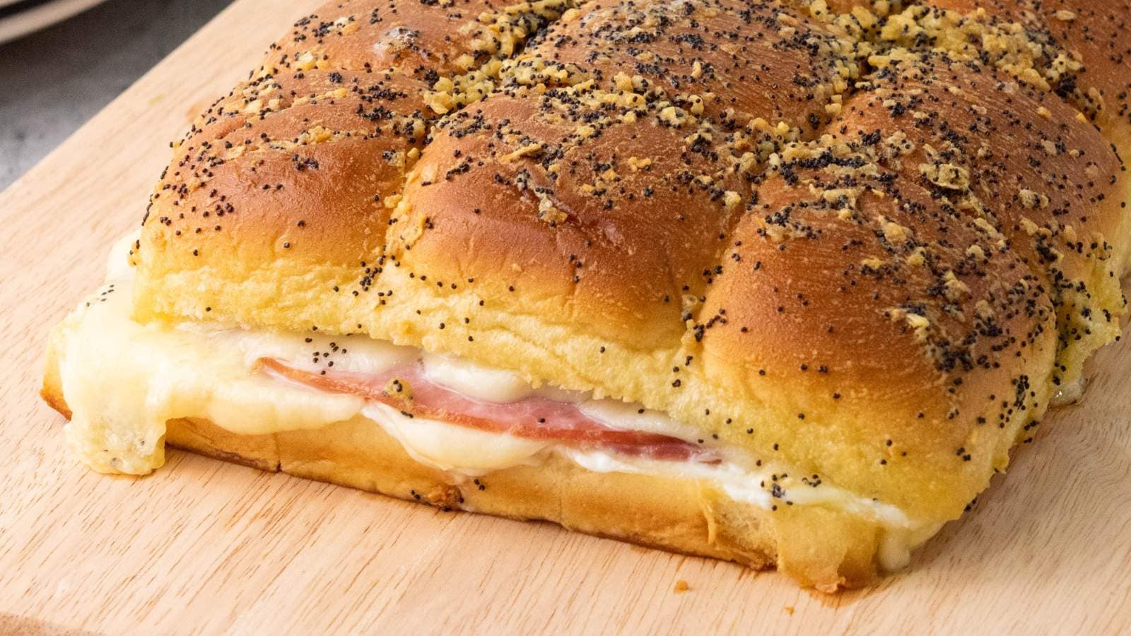 Ham and cheese sliders with poppy seeds and garlic topping on a wooden board.