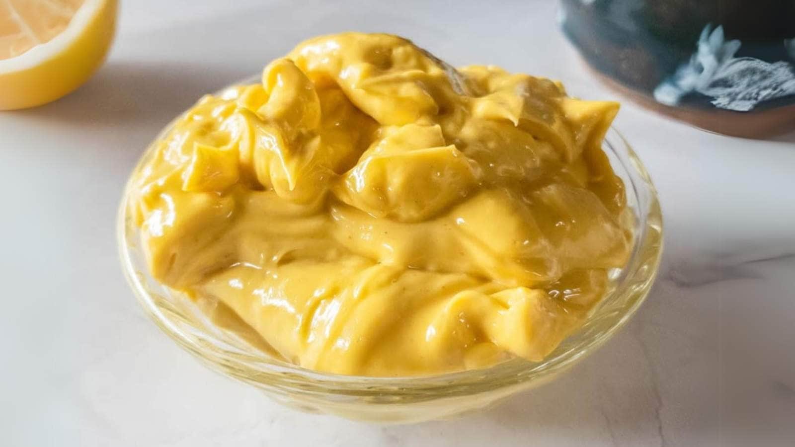 A small glass bowl filled with thick, yellow homemade mayonnaise sits on a white surface.