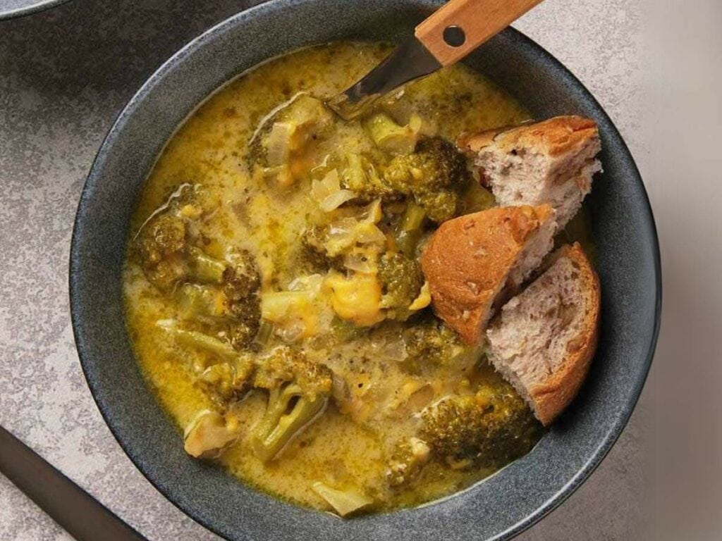 A bowl of panera broccoli cheddar soup with chunks of broccoli and a spoon.
