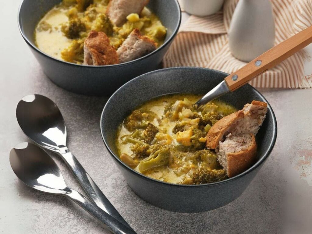 Two bowls of panera broccoli cheddar soup with bread pieces.