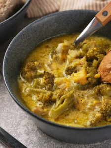A bowl of panera broccoli cheddar soup with chunks of broccoli and creamy broth, served with a piece of bread.