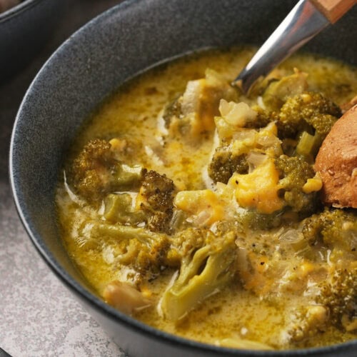 A bowl of panera broccoli cheddar soup with chunks of broccoli and creamy broth, served with a piece of bread.