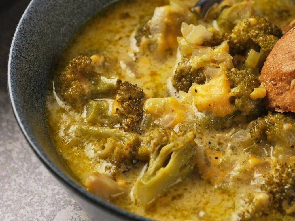 A bowl of panera broccoli cheddar soup with visible chunks of broccoli and cheese.