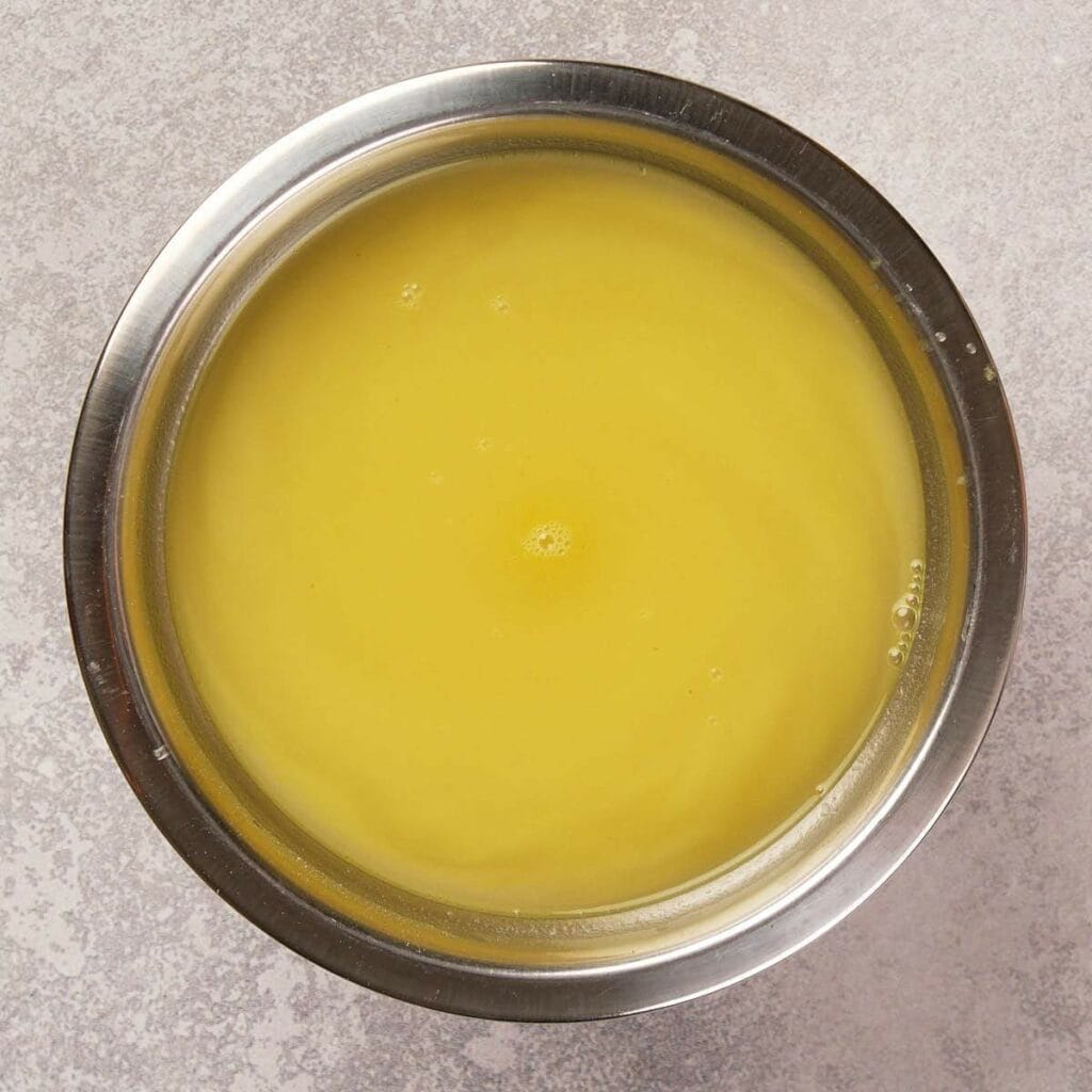 A stainless steel bowl filled with smooth, yellow liquid seen from above, placed on a light gray surface.