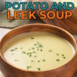A wooden bowl filled with creamy potato and leek soup, garnished with chopped green herbs, on a table.