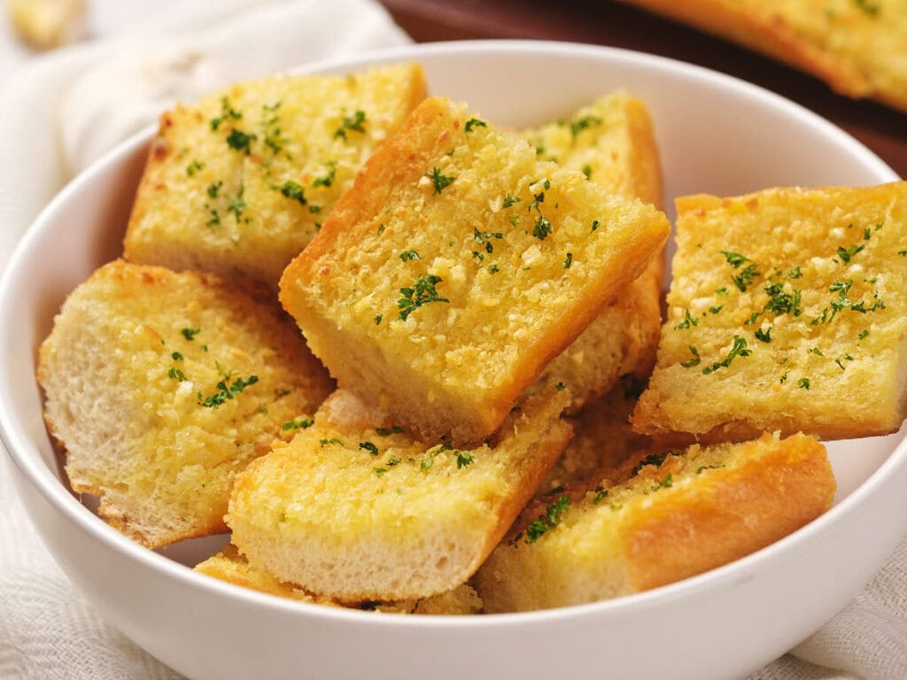 A bowl filled with sliced roasted garlic bread topped with chopped parsley.