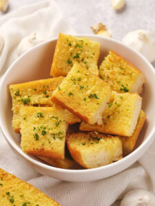 A bowl of roasted garlic bread cubes garnished with herbs.