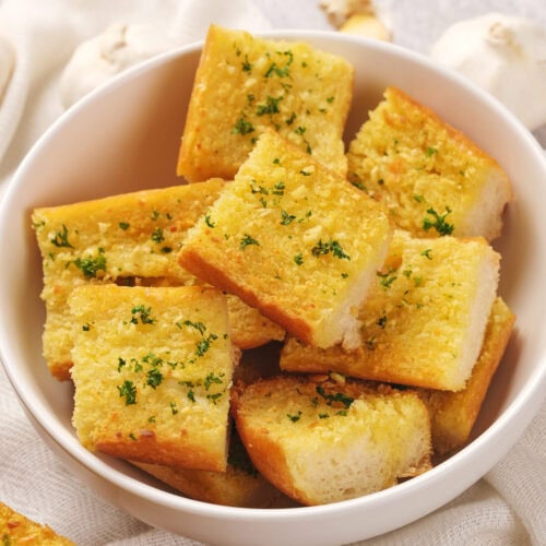 A bowl of roasted garlic bread cubes garnished with herbs.