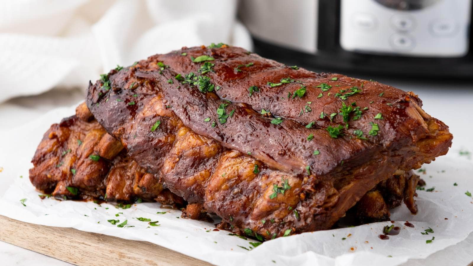 A cooked rack of baby back ribs garnished with chopped herbs sits on parchment paper.