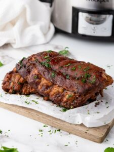 Baby back ribs garnished with chopped herbs sits on parchment paper atop a wooden cutting board.