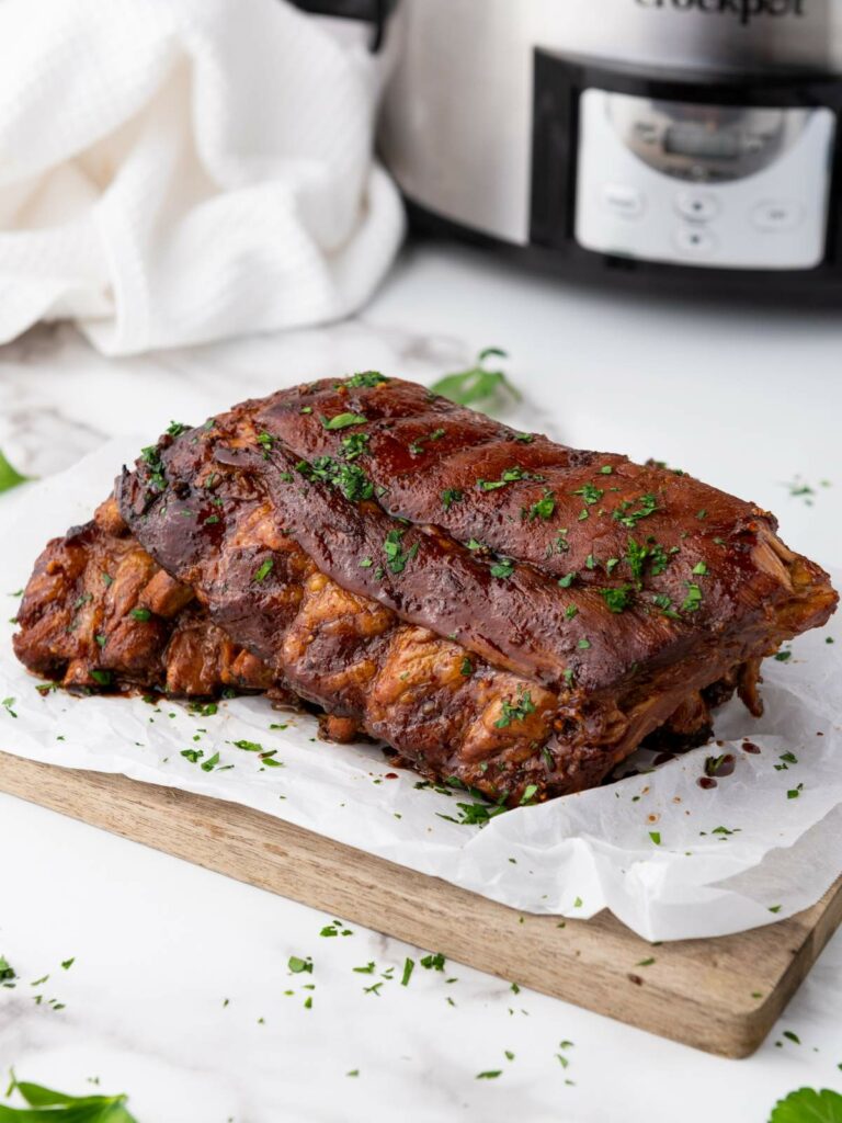 Baby back ribs garnished with chopped herbs sits on parchment paper atop a wooden cutting board.
