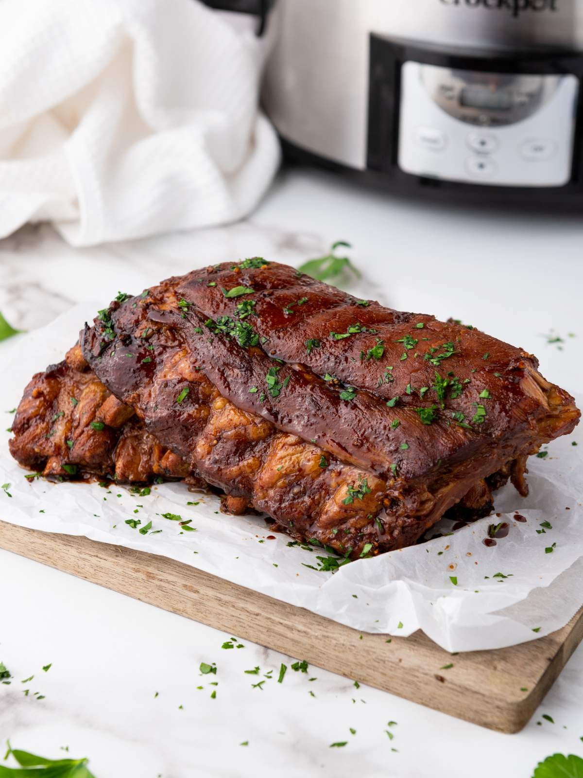 Baby back ribs garnished with chopped herbs sits on parchment paper atop a wooden cutting board.