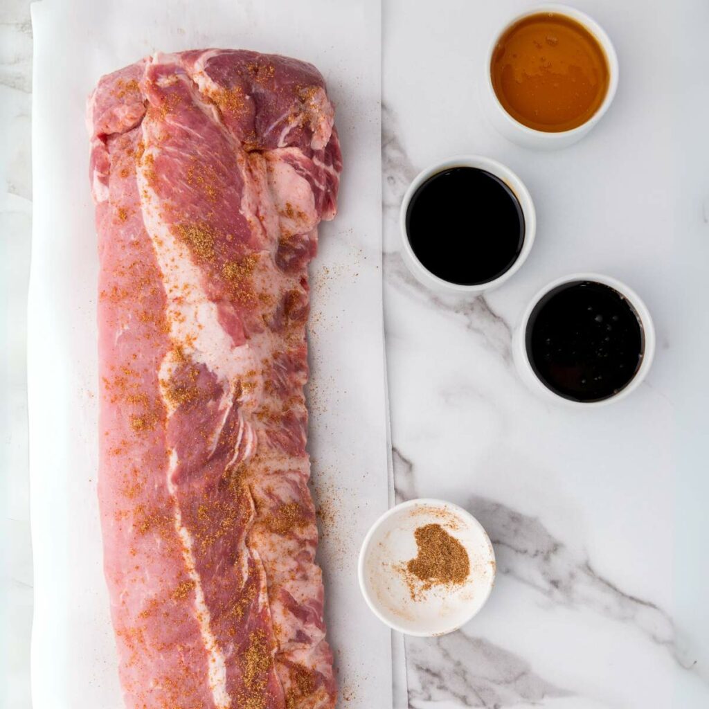 Raw pork tenderloin seasoned with spices on parchment paper.