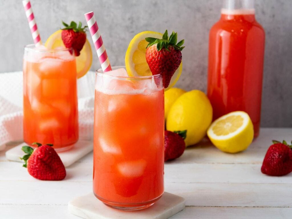 Two iced glasses of strawberry lemonade garnished with lemon slices and whole strawberries.
