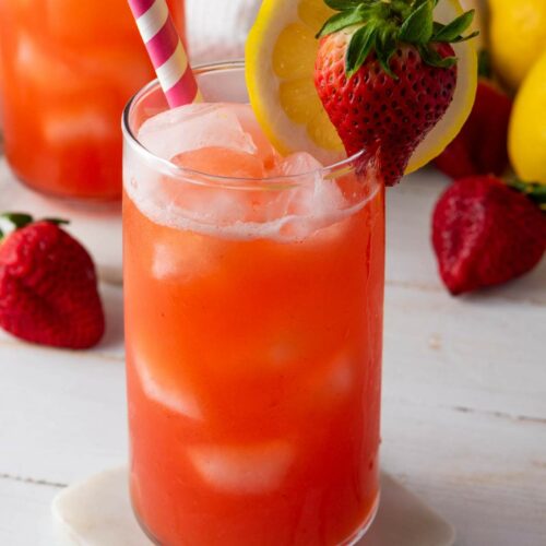 A glass of iced strawberry lemonade garnished with a lemon slice and whole strawberry.