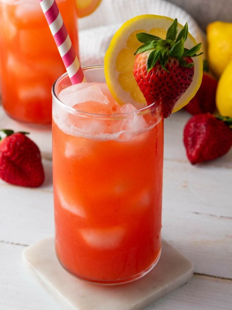A glass of iced strawberry lemonade garnished with a lemon slice and whole strawberry.