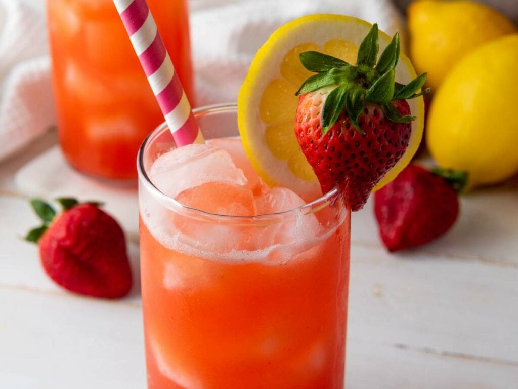 A glass of iced strawberry lemonade garnished with a lemon slice and a strawberry.