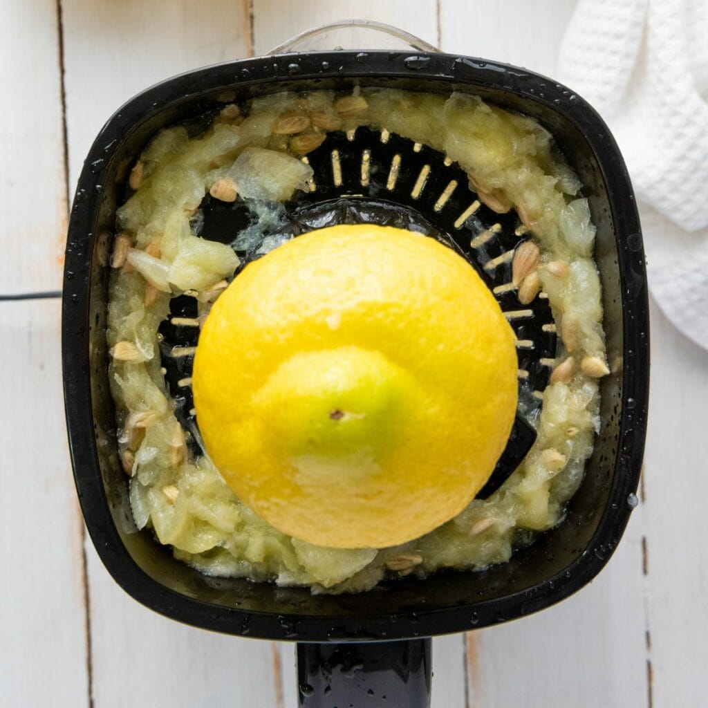 A lemon being juiced on a black manual citrus juicer, with pulp and seeds collected around the edges.