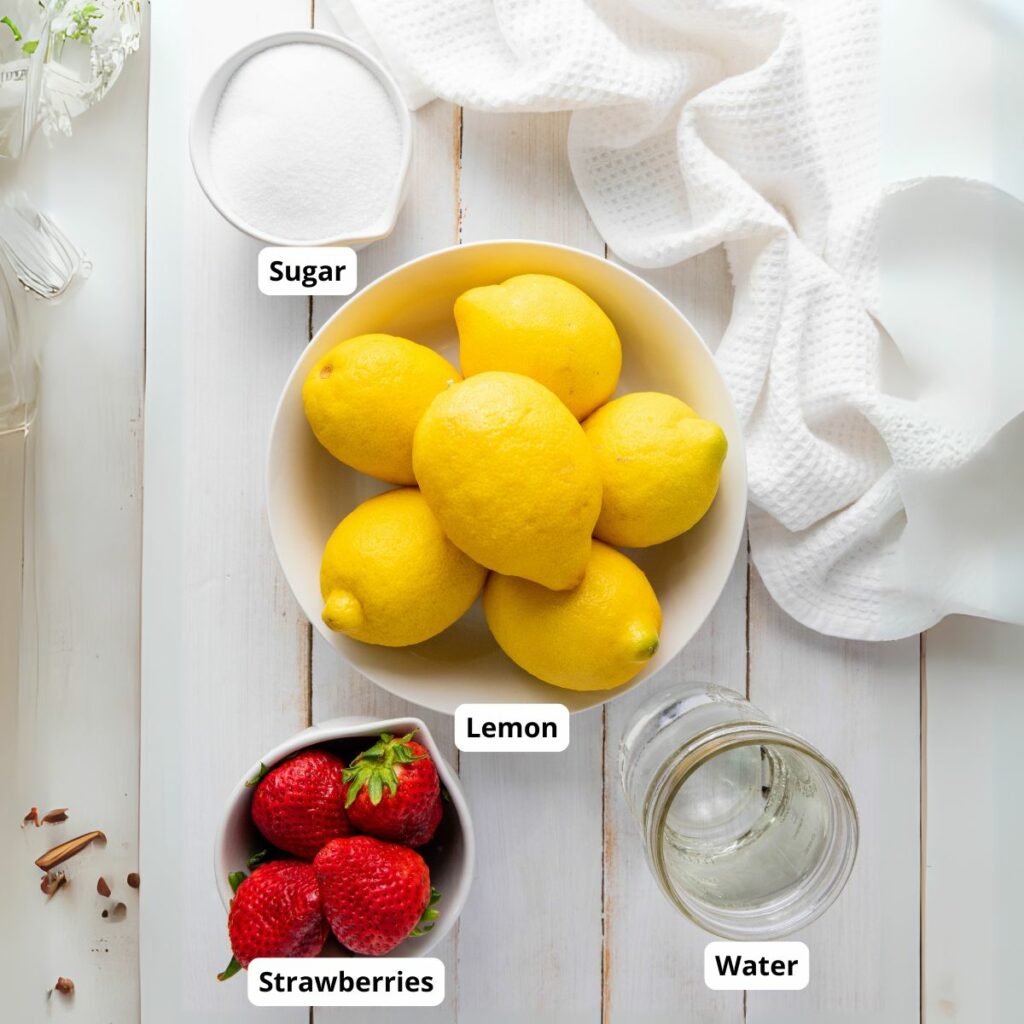 A bowl of lemons, a cup of sugar, a cup of strawberries, and a glass of water are arranged on a white surface.