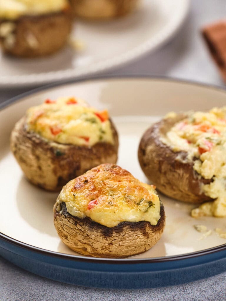 Three baked mushrooms stuffed with a cheesy filling sit on a round plate.
